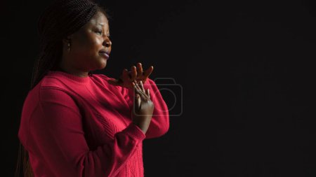 Photo for Side-view portrait of female model performing timeout, pause motion on camera. African american woman in black background displaying a t shape stop symbol with her arms, indicating no. - Royalty Free Image