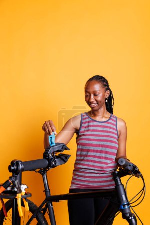 La joven ciclista de etnia afroamericana inspecciona componentes rotos de bicicletas con herramientas. Mujer negra experta y precisa arreglando el soporte de reparación para ajustes y mantenimiento de bicicletas.
