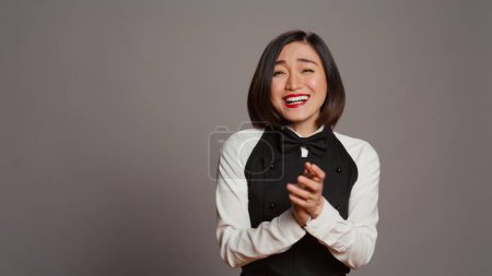 Photo for Asian server applauding someone and cheering for success, saying congratulations in front of camera. Waitress in formal uniform clapping hands, doing standing ovation gesture. Camera B. - Royalty Free Image