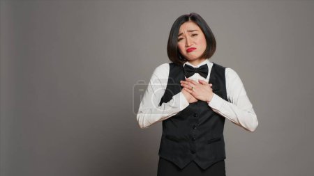 Photo for Front desk staff feeling bored and sleepy on camera, dealing with burnout and confusion over grey background. Receptionist with uniform and tie being exhausted and uncertain. Camera A. - Royalty Free Image
