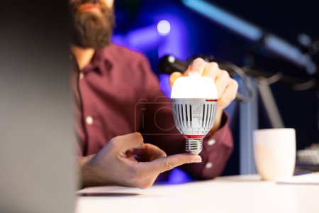 Close up shot of smart light bulb reviewed by tech enthusiast in studio discussing with audience about home improvement, telling viewers latest news in WiFi home automation industry