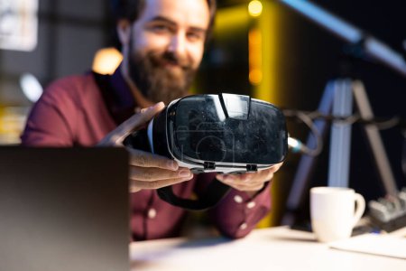 Téléchargez les photos : Gros plan sur les lunettes VR futuristes tenues par un spécialiste de la technologie qui les examine pour les téléspectateurs. Internet star filming technologie canal vlog pour les amateurs de gadgets, mettant en valeur la réalité virtuelle casque - en image libre de droit