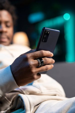 Photo for Close up shot on smartphone held by person texting internet friends, enjoying himself at home. Focus on phone used by african american man in blurry background to enjoy leisure time - Royalty Free Image