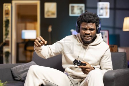 BIPOC-Spieler schreit nach dem verlorenen Videospiel und macht Frust-Gesten. Wütender Gamer auf Couch in Wohnung bereit, Gamepad-Controller zu werfen, wütend nach Spielempfang über Nachricht
