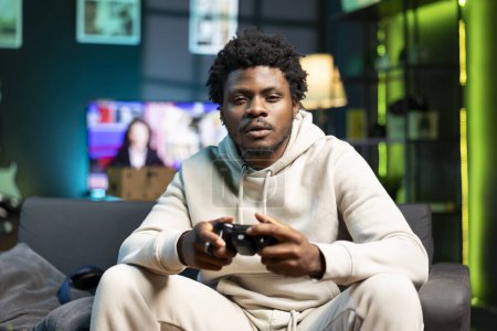 Bored person plays online videogame, spamming attack buttons on gamepad. Gamer in neon lit apartment participating in internet esports competition, sitting on couch and playing on gaming console