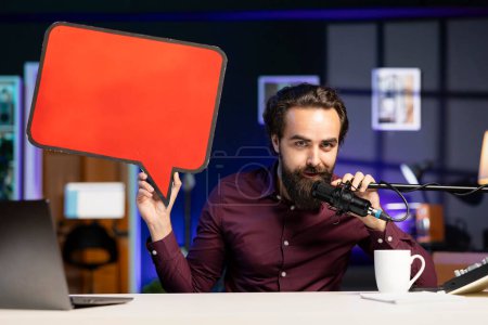 Influencer filming content, holding empty copy space sign, talking in professional microphone. Online star using cardboard bubble speech cutout to do influencer marketing, speaking in high tech mic
