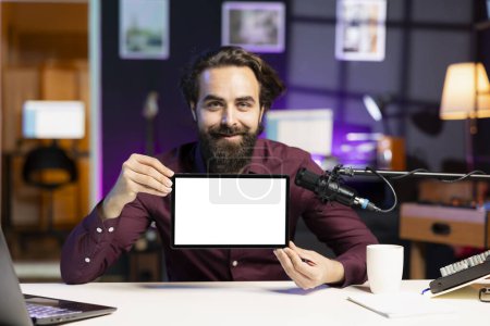 Portrait of smiling man in studio filming tech tutorial on how to do maintenance on mockup broken tablet. Online show host teaching subscribers how to open and fix isolated screen digital device