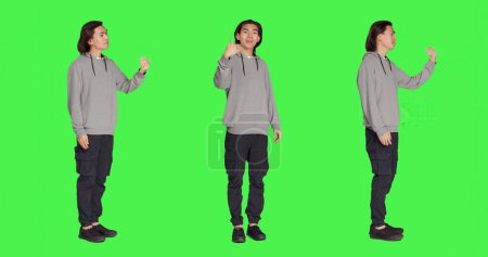 Hombre asiático pidiendo a la persona que venga, animando a la gente a acercarse mientras está de pie contra la pantalla verde de cuerpo entero. Adulto en ropa casual instando a alguien a acercarse a él.