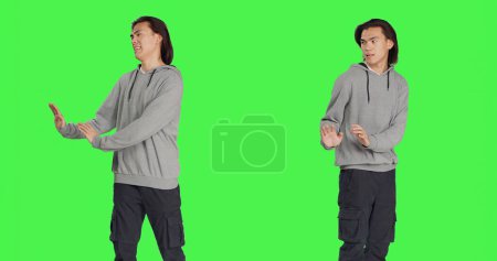 Male model pretending to push something aside, expressing rejection or refusal in studio. Young man mimicking dismissal over isolated greenscreen background, stop symbol.
