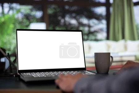 Photo for Wealthy shareholder relaxes in his posh mountain chalet and looking at white screen template on notebook. Foreign chairman works with blank mockup display on laptop from luxury forest villa. - Royalty Free Image