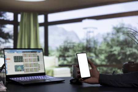 Der einflussreiche CEO hält ein Telefon mit weißem Bildschirm in der Hand und arbeitet von seinem luxuriösen Alpenresort aus. Reicher Unternehmer untersucht Finanzressourcen und leeres Display in Smartphone-App.