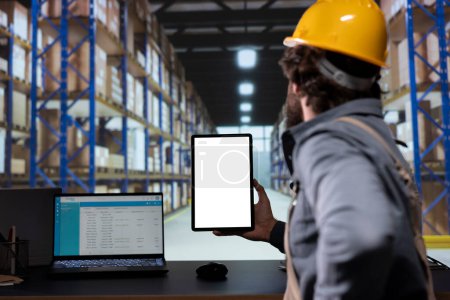 Depot worker examining stock checklist and tablet with white screen, working on delivery and shipment with cargo logistics. Supervisor holding device with blank display copyspace, retail industry.