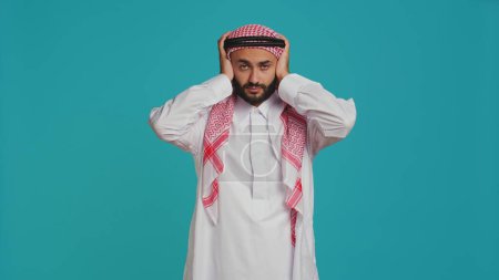 Photo for Adult does three wise monkeys sign on camera, wearing muslim traditional clothes and scarf. Young person covering his eyes, mouth and ears to illustrate metaphor symbol, concept. - Royalty Free Image