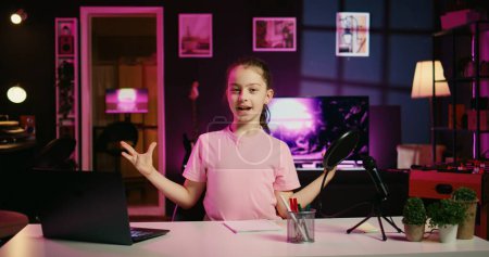 Photo for Happy child and her loving mom recording family vlog intro on online platforms. Young smiling daughter and parent warmly welcoming dedicated gen Z fans, filming in home studio with pink neon lighting - Royalty Free Image