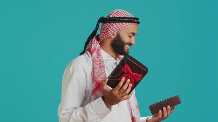 Photo for Arab person opening giftbox with ribbon, receiving beautiful present on his birthday. Middle eastern happy guy feeling excited about gift wrapped with box, holiday package. - Royalty Free Image