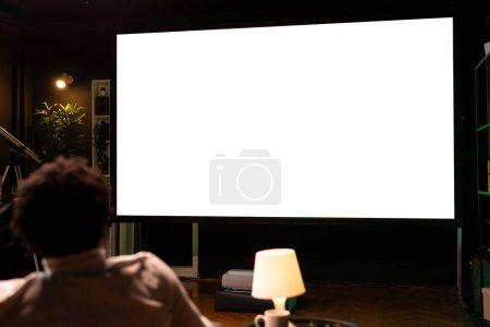 Person using isolated screen large smart TV to binge series on subscription based streaming services, having fun. BIPOC man relaxing, enjoying VOD shows on mockup television display