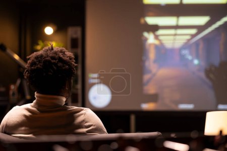 BIPOC-Mann spielt Singleplayer-Videospiele im Breitbildfernseher und entspannt sich nach einem langen Arbeitstag. Gamer genießen Science-Fiction-Ego-Shooter-Spiel auf Spielkonsole, schießen Feinde