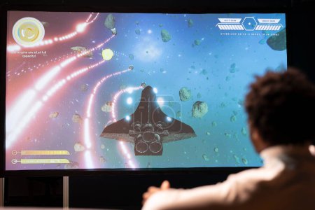 Man plays science fiction singleplayer game with overlay HUD showing health bars and minimap on ultrawide smart TV screen. Player enjoying high quality graphics in cloud gaming streamed videogame