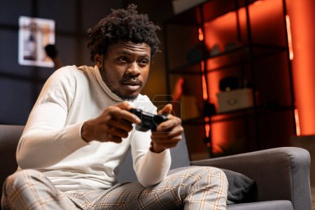 Photo for Gamer playing videogames on console late at night in orange neon illuminated room, struggling to stay awake. Man using joystick controller to try and finish game mission before going to sleep - Royalty Free Image