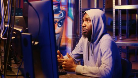 Zoom in shot on african american hooded hacker targeting vulnerable unpatched connections, seeking to compromise digital devices and steal valuable sensitive data from them