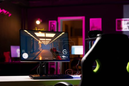 Professionelle Gaming-Studio leeren Raum mit Neonlicht und RGB beleuchteten leistungsstarken Computer, Ego-Shooter-Spiel auf dem Bildschirm offen gelassen. FPS-Videospiel auf PC-Display in Wohnung spät in der Nacht