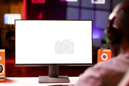 Professional streamer looking at isolated screen monitor, competing in online videogame, streaming live at home. Mockup display used by man playing on PC, using headphones to talk, close up