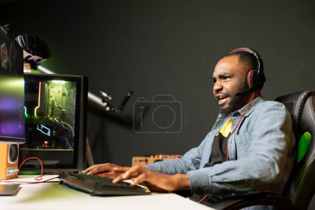 Excited man playing intense videogame on gaming PC at computer desk, enjoying day off, having fun. Focused gamer battling enemies in online multiplayer shooter, feeling strong emotions