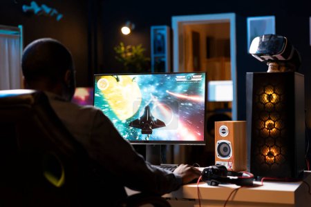 African american player in neon illuminated apartment paying close attention to computer screen during videogame competitive match. BIPOC person competing in internet esports tournament