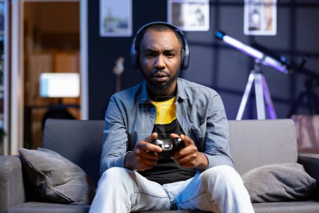 Photo for Portrait of irritated gamer upset after losing in online multiplayer videogame played using controller. Man frustrated after seeing game over message while playing on console - Royalty Free Image