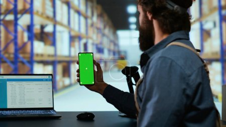 Delivery industrial advisor shows greenscreen display in warehouse storage room, working on cargo logistics for new order shipment. Depot supervisor holds isolated chromakey device.