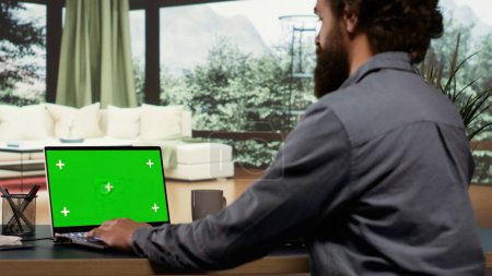 Photo for Businessman looks at greenscreen template on pc, getting cozy inside his posh opulent mountain villa. Wealthy entrepreneur examining isolated copyspace display on laptop, billionaire work. - Royalty Free Image