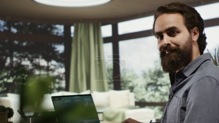 Entspannter reicher Mann mit Laptop im Luxus-Ferienhaus, der online geht, um Ertragstrends für Finanzinvestitionen zu sehen. Unternehmer Telearbeit aus seiner modernen Nobelvilla im Wald.