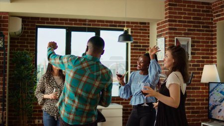 Téléchargez les photos : Mélange multiculturel d'invités à la fête appartement partageant rire et mouvements de danse, créant une atmosphère vibrante dans le salon. Des amis heureux dansent sur des rythmes électroniques pendant le week-end - en image libre de droit