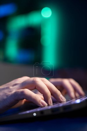 Close up shot of laptop used by freelancer working from home in RGB lit apartment typing on keyboard. Focus on notebook used by teleworking accountant writing audit on couch in blurry background