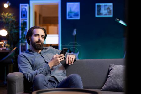 Man lounged on couch texting friend on smartphone, inviting him to watch movie on streaming service. Person at home discussing with mate on mobile phone, recommending TV show