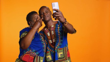 Téléchargez les photos : Heureux couple afro-américain capturant un moment mignon en studio, prenant des photos sur smartphone et profitant d'activités de loisirs. Les personnes mariées romantiques prennent des photos pour des souvenirs au téléphone. - en image libre de droit
