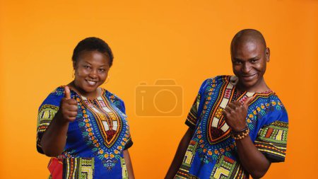 Photo for African american couple showing thumbs up symbol on camera, feeling positive and presenting their satisfaction. Married people expressing approval and giving like sign in studio. - Royalty Free Image