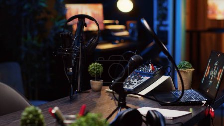 Panning shot of desk in home production studio with podcast equipment technology recording sound and 3D animations running on laptop screen. Professional broadcasting space in apartment