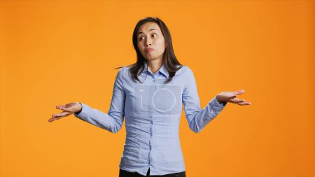 Photo for Doubtful model raising shoulders over orange background, showing doubt and being clueless about answer. Young filipino person acting uncertain and confused standing in front of camera. - Royalty Free Image