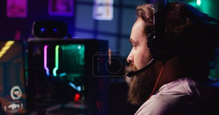 Man using headphones microphone to talk with teammates while playing FPS videogame with gun shooting laser bullets. Gamer chatting with internet friends while enjoying SF game, close up