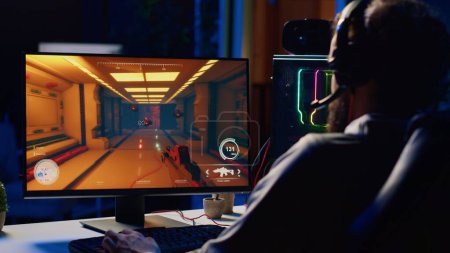 Hombre relajante jugando futurista videojuego de ciencia ficción en PC en el escritorio de la computadora tarde en la noche. Gamer disparar a los enemigos con láser en línea multijugador shooter en primera persona