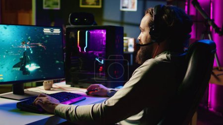 Mann in neonbeleuchteter Wohnung hat Spaß und lacht, während er unterhaltsames Videospiel mit Online-Freunden spielt, gemeinsam Raumschiff durch Galaxie fliegt und über Kopfhörermikrofon kommuniziert