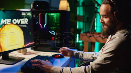 Photo for Man upset after losing while playing online multiplayer spaceship videogame, showing sarcastic smile in frustration. Gamer feeling disappointed after receiving game over message - Royalty Free Image