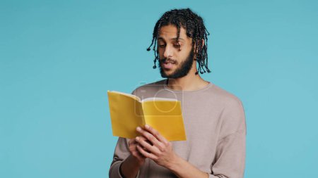Middle Eastern man reading book from publisher aloud, telling story, enjoying hobby. BIPOC person narrating literature novel, doing critique essay, isolated over studio background, camera B