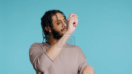 Photo for Middle Eastern conductor performing classical music concert following imaginary sheet music. Man doing delicate swinging hand motions, pretending to conduct orchestra, studio background, camera B - Royalty Free Image