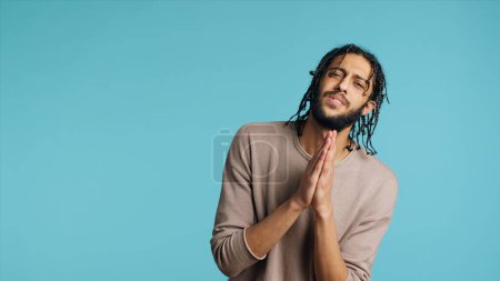 Photo for Pious Middle Eastern man praying to his god, asking for forgiveness, feeling desperate. Spiritual BIPOC man doing worship hand gesturing, confessing, begging for pardon, studio background, camera A - Royalty Free Image