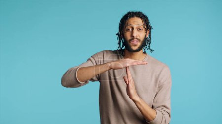 Assertive Middle Eastern man asking for timeout, doing hand gestures. BIPOC person doing pause sign gesturing, wishing for break, isolated over blue studio background, camera A
