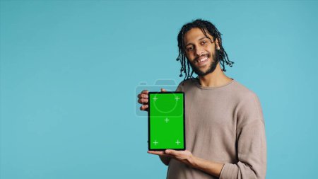 Photo for Joyful man holding green screen tablet, showing positive emotion. Upbeat person presenting chroma key device, doing recommendation, isolated over studio background, camera A - Royalty Free Image