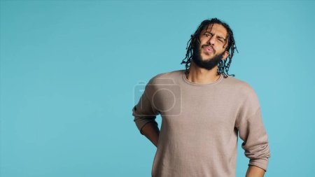Photo for Hurt Middle Eastern man screaming from pain, suffering from back injury, having health problems. Injured BIPOC person feeling uncomfortable ache, yelling, studio background, camera A - Royalty Free Image