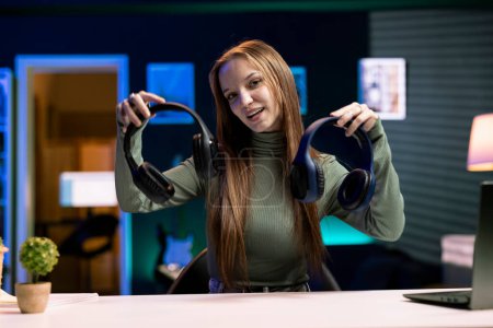 Cheerful gen Z influencer in studio films headphones comparison video review for audience. Upbeat girl hosts technology online show, unboxing music listening devices for her fanbase